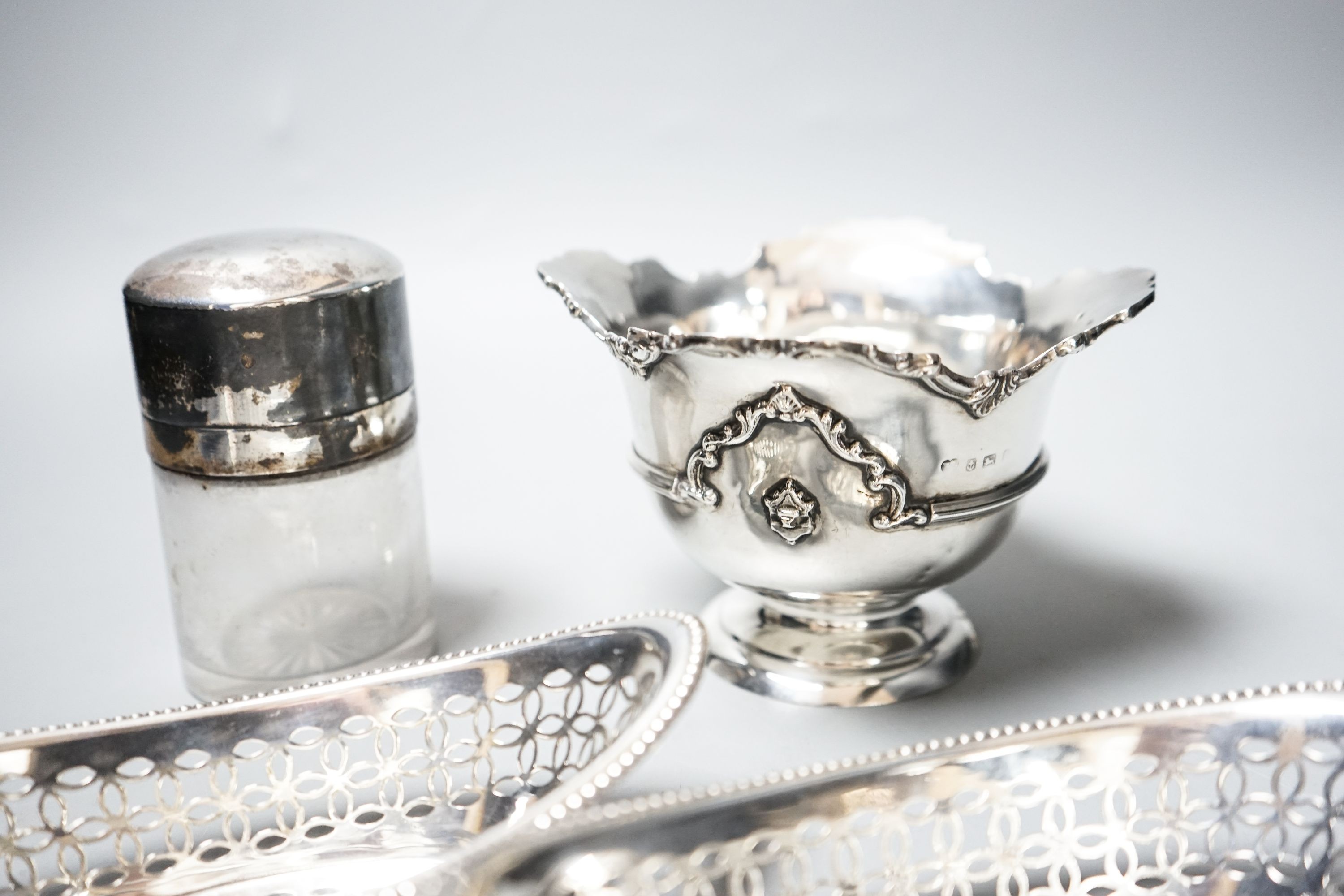 A pair of Edwardian silver oval bon bon dishes, a George V silver sugar bowl and a silver mounted glass smelling salts bottle.